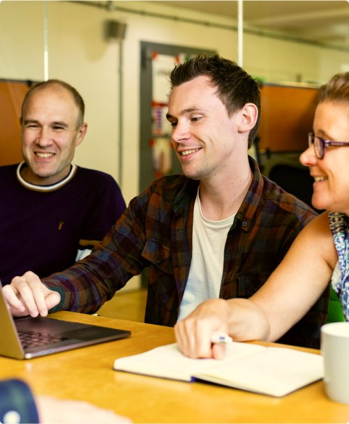 Three colleagues reviewing work on a laptop